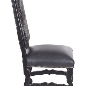 Pu&ograve; includere: Una sedia da pranzo nera con schienale imbottito in pelle di mucca e seduta in pelle nera. La sedia ha una struttura in legno intagliato con finitura anticata e bordi con chiodi decorativi.