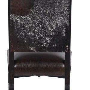 Pu&ograve; includere: Una sedia da pranzo nera con una seduta in pelle marrone e uno schienale in pelle di mucca nero e bianco.