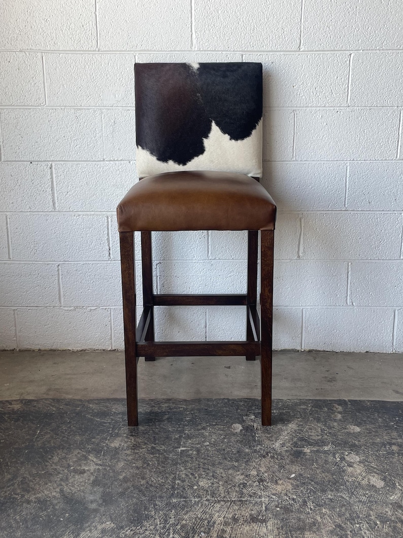 May include: A brown leather bar stool with a black and white cowhide seat.