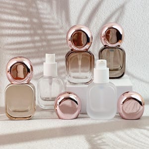 Clear and frosted white 20ml perfume bottles with white spray pumps, some lying on their side.