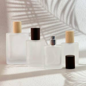 May include: Four frosted glass perfume bottles with wooden and dark brown caps. One bottle has a silver spray nozzle. The bottles are rectangular and vary slightly in size. The background is white with shadows.
