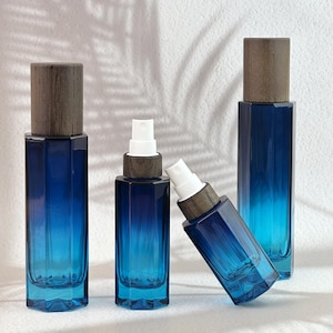 May include: Four blue glass spray bottles with wooden caps. The bottles have a rectangular shape with a gradient color from dark blue to light blue. The spray nozzles are white.