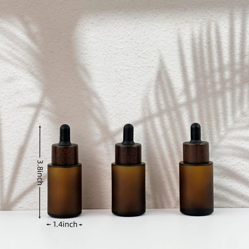 May include: Three amber glass dropper bottles with black droppers and wooden caps. Each bottle is 3.8 inches tall and 1.4 inches wide. The bottles are arranged in a row on a white surface.