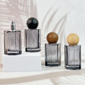 May include: Four grey glass perfume bottles with wooden and silver tops. The bottles are rectangular with a faceted design. Two bottles have wooden sphere tops, one has a black sphere top, and one has a silver spray top.