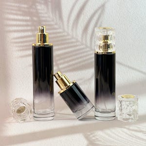 May include: Several glass perfume bottles with gold-colored tops and a gradient black to clear design. One bottle is lying on its side. Two clear, decorative caps are also present.