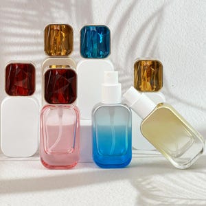 May include: An assortment of perfume bottles with square, jewel-toned caps in shades of red, gold, and blue. The bottles are clear, with a gradient of pink and blue hues. Some bottles are upright, while others are angled.