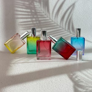 Könnte beinhalten: Fünf rechteckige Parfümflakons aus Glas mit silbernen Sprühverschlüssen. Die Flakons haben Farbverläufe in Gelb, Grün, Pink, Rot und Blau. Einige der Flakons sind in verschiedenen Winkeln geneigt aufgestellt.