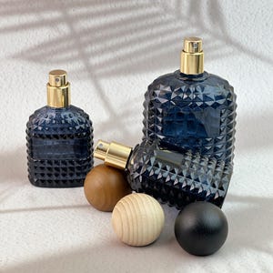 Three navy blue diamond cut glass spray bottles, one tilted to show spray pump, with dark/light/black wood caps on white textured background.
