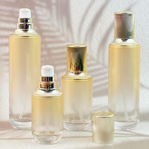 May include: Several clear glass cosmetic bottles with gold-colored accents and white spray nozzles. The bottles vary in size and shape, with a gradient yellow-to-clear finish. One bottle has a gold cap.