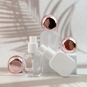 White and clear 20ml perfume bottles with rose gold caps removed, showing the spray pumps and bottle details.