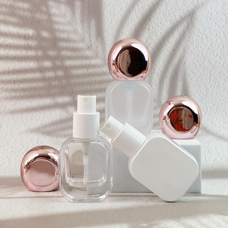 White and clear 20ml perfume bottles with rose gold caps removed, showing the spray pumps and bottle details.