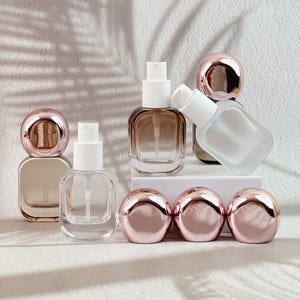 Champagne gold, clear, and gradient brown 20ml perfume bottles with rose gold caps and white pumps, displayed on a light background.