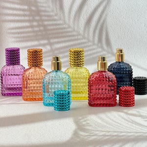 Puede incluir: Una colección de coloridos frascos de perfume de vidrio con patrones de diamantes texturizados. Los frascos vienen en varios colores, incluyendo púrpura, naranja, azul, amarillo, rojo y azul marino. Cada frasco tiene un pulverizador dorado y una tapa texturizada a juego.