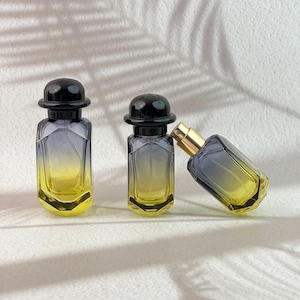 May include: Three perfume bottles with a gradient design. The bottles transition from yellow to gray, with black caps and gold spray nozzles. One bottle is tilted, showcasing the design.