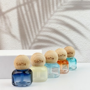 May include: Five small, glass bottles with wooden tops, each containing a different colored liquid. The bottles are arranged in a row, with the colors ranging from blue to clear to orange and blue. The wooden tops are engraved with the word "Smile".