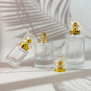 Peut inclure: Plusieurs flacons de parfum en verre transparent avec des vaporisateurs dorés et des bouchons décoratifs. Les flacons sont cylindriques avec des détails côtelés verticaux. Les bouchons ont un design géométrique.