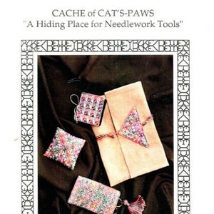 May include: A set of four needlework tools, including a pincushion, needlecase, scissor case, and a clutch purse. The tools are all decorated with colorful embroidery and are arranged on a dark brown fabric background. The text "CACHE of CAT'S-PAWS" and "A Hiding Place for Needlework Tools" is displayed at the top of the image.