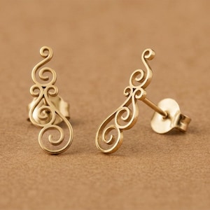 May include: A pair of gold-toned stud earrings featuring an elongated, openwork design composed of multiple interconnected swirls and scrolls. Each earring includes a standard post backing and is crafted with a smooth, polished metallic finish.