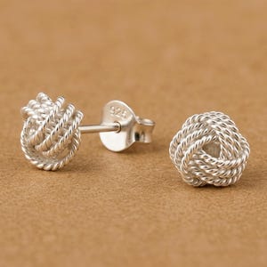 May include: A pair of sterling silver stud earrings featuring a spherical love knot design made of twisted wire. One earring shows the post and a butterfly back with the hallmark 925 stamped on the metal, while the other sits beside it.