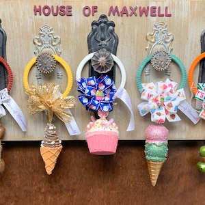 May include: Five decorative door hangers with different themes. Each hanger features a ribbon with a bow, a small ornament, and a tag that says "House of Maxwell". The themes include fall, ice cream, cupcake, and a Christmas theme.