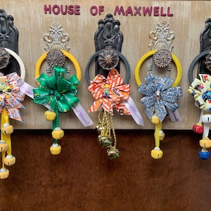 May include: Five door hangers with yellow, green, orange, blue, and yellow and red bows with bells. The door hangers are decorated with construction vehicle themed fabric. The sign above the door hangers reads "House of Maxwell".