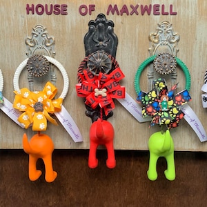 May include: Five colorful dog-shaped hooks with bows and ribbons hanging on a wooden door with the text "HOUSE OF MAXWELL".