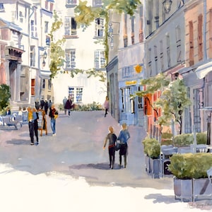 May include: Watercolor painting of a European street scene. Buildings in shades of white, blue, and pink line the street. People are walking and sitting at outdoor cafes. Trees and greenery add color to the scene.