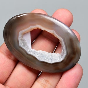 Op de afbeelding: Een grijze agaatgeode met een natuurlijke opening, die een wit kristal interieur onthult. De geode is glad en gepolijst, met een natuurlijke, ovale vorm.
