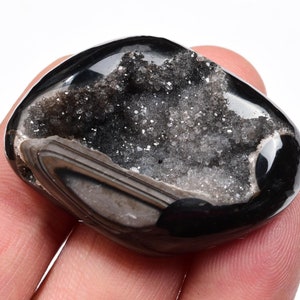 May include: Black agate geode with a crystal-lined interior. The geode is smooth and polished, with a dark grey exterior and a white crystal interior.
