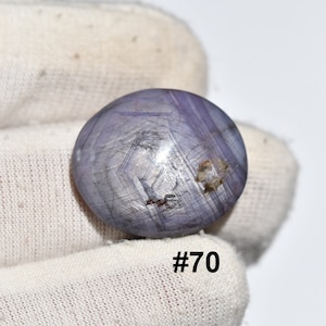 May include: Four purple star sapphire cabochons with silver inclusions. The stones are labeled #70, #71, #72, and #73.