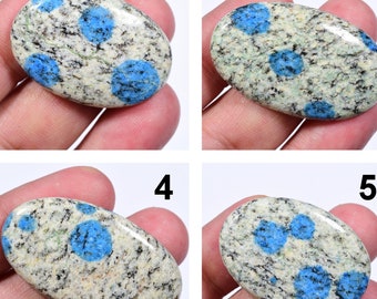 May include: Nine oval-shaped blue and white speckled stones with blue spots. The stones are arranged in three rows of three.