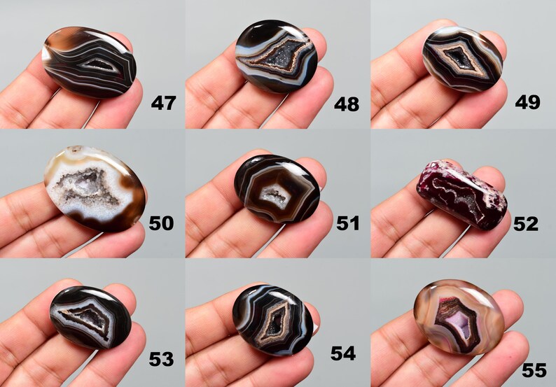 Op de afbeelding: Assortiment van 10 ovale agaat cabochons met verschillende patronen in zwart, wit en bruin. De cabochons worden getoond op een hand.