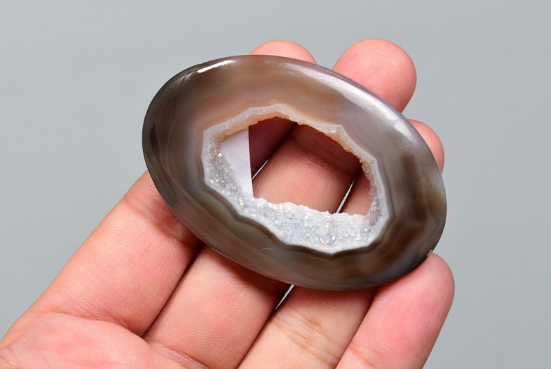 Op de afbeelding: Een grijze agaatgeode met een natuurlijke opening, die een wit kristal interieur onthult. De geode is glad en gepolijst, met een natuurlijke, ovale vorm.