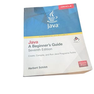 May include: A softcover technical book titled Java: A Beginner's Guide, Seventh Edition by Herbert Schildt. The cover features a blue and white geometric design, the Oracle logo, the Java coffee cup icon, and the text: Create, Compile, and Run Java Programs Today.