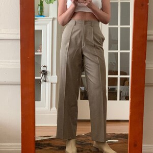May include: A person wearing a white tank top and beige wide-leg pants with a high waist. The pants have pleats and a straight leg.