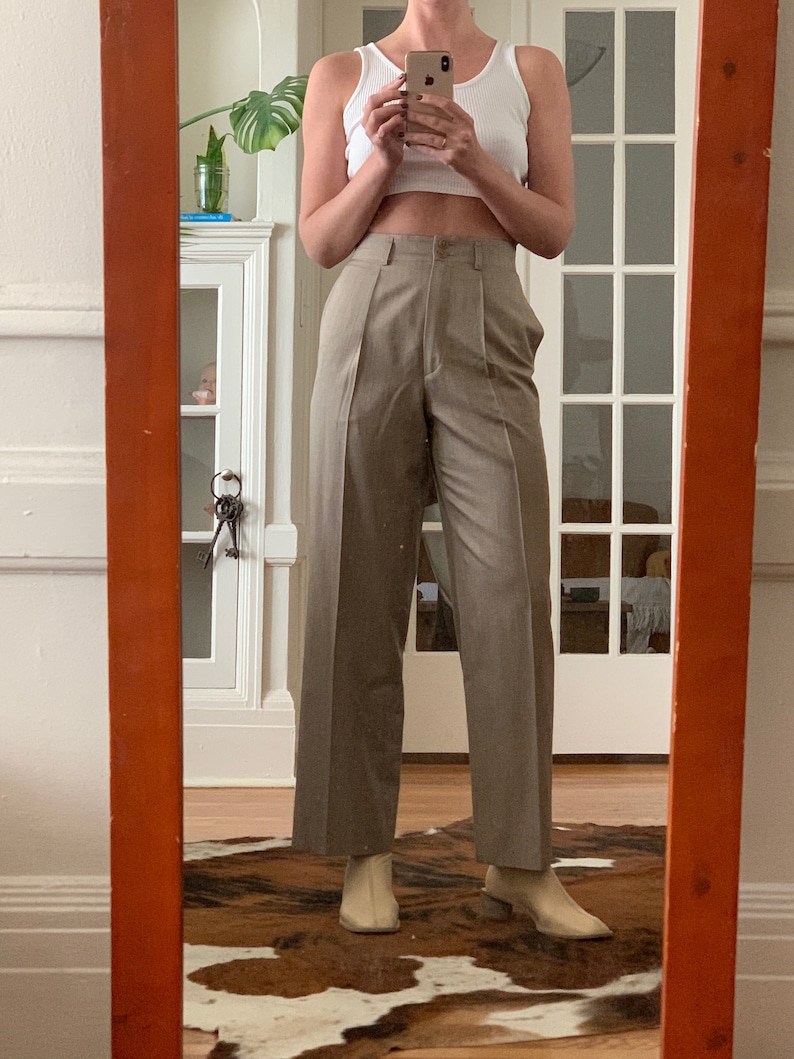 May include: A person wearing a white tank top and beige wide-leg pants with a high waist. The pants have pleats and a straight leg.