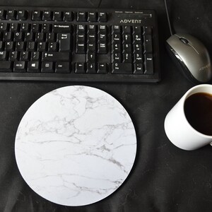 Peut inclure: Un tapis de souris en marbre blanc avec un clavier noir, une souris d'ordinateur noire et une tasse à café blanche avec du café sur une surface noire.