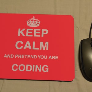 May include: Red mouse mat with the text "Keep Calm and Pretend You Are Coding" in white lettering. A crown graphic is above the text. A black computer mouse is to the right of the mouse mat.