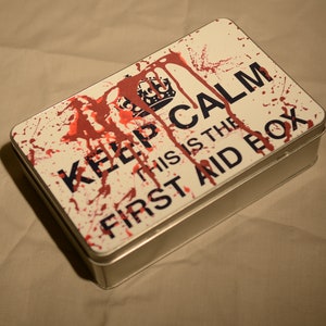 May include: A white metal first aid box with red blood splatter and the text "Keep Calm This Is The First Aid Box".