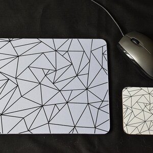 May include: A computer mouse, mouse mat, and coaster set. The mouse mat and coaster are white with a black geometric pattern. The mouse is silver and connected to a wire.