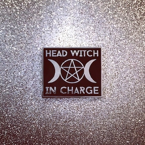 May include: Black enamel pin with a silver pentagram and crescent moons, and the text "Head Witch In Charge".