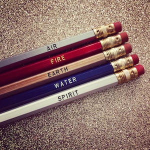 May include: Five pencils with gold trim and eraser tops, stacked on top of each other. The pencils are labeled "AIR", "FIRE", "EARTH", "WATER", and "SPIRIT".