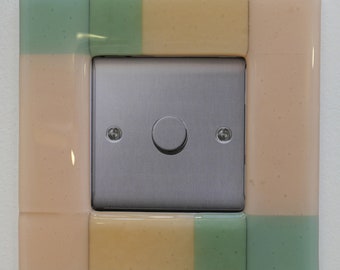 Kiln formed glass light switch surround in opaque salmon pink.
