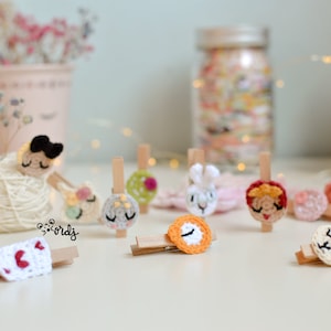 Puede incluir: Una colección de 10 amuletos de ganchillo de colores con diferentes diseños, incluyendo un conejito, una flor, un reloj y un corazón. Los amuletos están unidos a pinzas de madera.