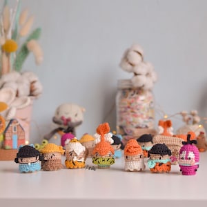 Puede incluir: Una colección de pequeñas muñecas de ganchillo hechas a mano en varios colores y diseños. Las muñecas tienen sombreros, bufandas y otros accesorios. El fondo incluye elementos decorativos como tallos de algodón y luces de hadas, creando una escena caprichosa.