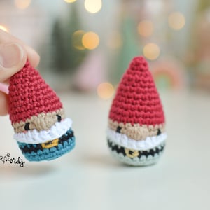 Op de afbeelding: Twee gehaakte gnomen met rode mutsen, witte baarden en zwarte riemen. De ene gnom heeft een blauw en zwart patroon, de andere een grijs en zwart patroon.