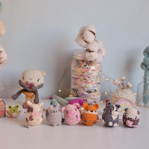 May include: A collection of handmade crochet animal figurines in various colors. The figurines include a frog, cow, cat, pig, fox, dog, and bear. The animals are arranged on a white surface with a light blue background.