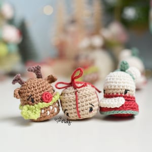 May include: Four crocheted Christmas ornaments: a reindeer with a green scarf, a wrapped gift with a red ribbon, a snowman with a red hat, and a white ornament with a green top.