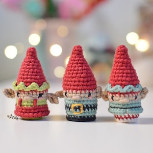 Puede incluir: Tres adornos de gnomo de crochet con detalles rojos, verdes y azules. Los gnomos tienen caras blancas y ojos negros.