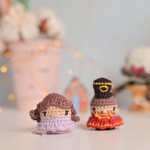 May include: Two crocheted dolls, one with brown hair and a purple dress, the other with a black hat and a red dress.